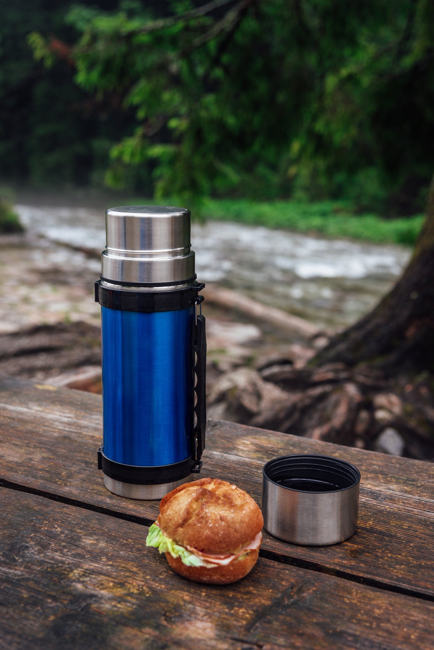 Camping table by the river with coffee and a sandwich