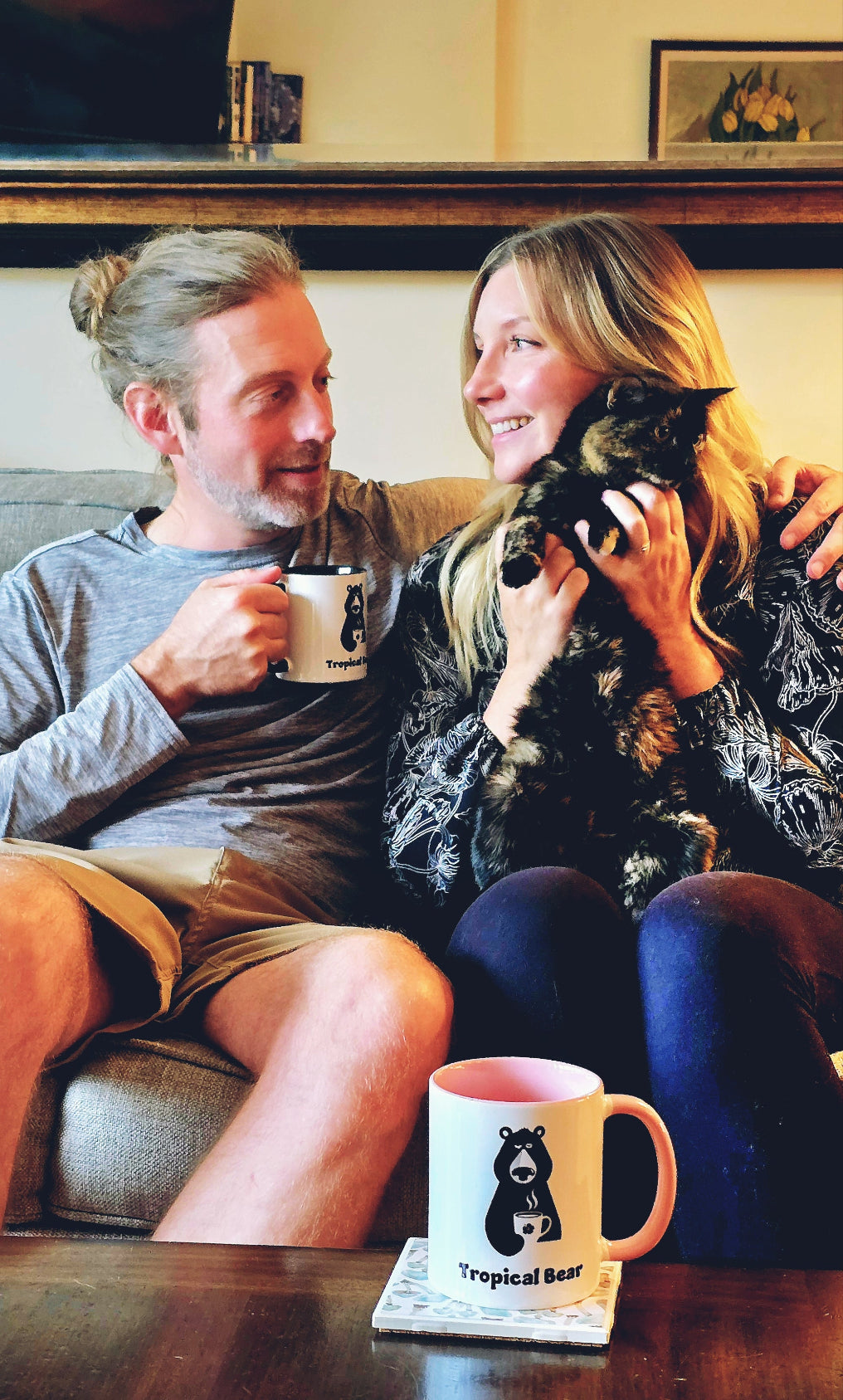 Monica and Austin look at each other while enjoying a cup of single-origin Ethiopia coffee on their couch with their kitty.