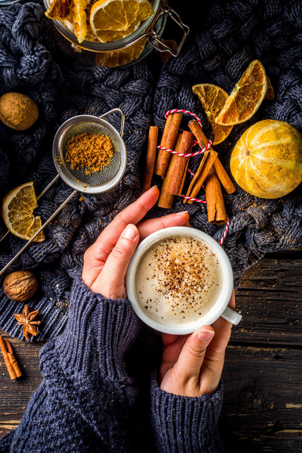 Sweater weather. Hands holding a cup of the Pumpkin Spice Specialty Grade Coffee on a table with peeled orange, cinnamon.