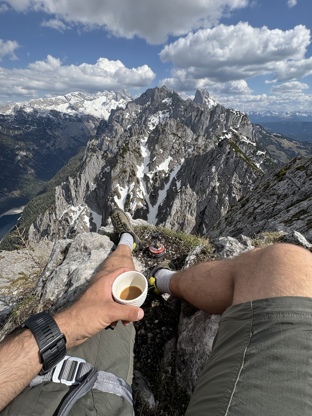 Person sitting on a mountain peak with a scenic view of snow-capped mountains while drinking Elevation Kick coffee.