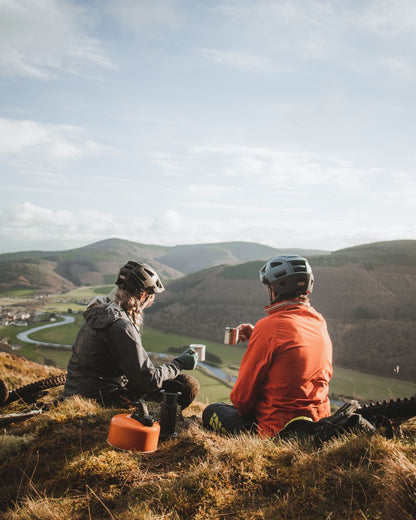 Two people sitting on a hilltop with scenic views and mountains in the background.