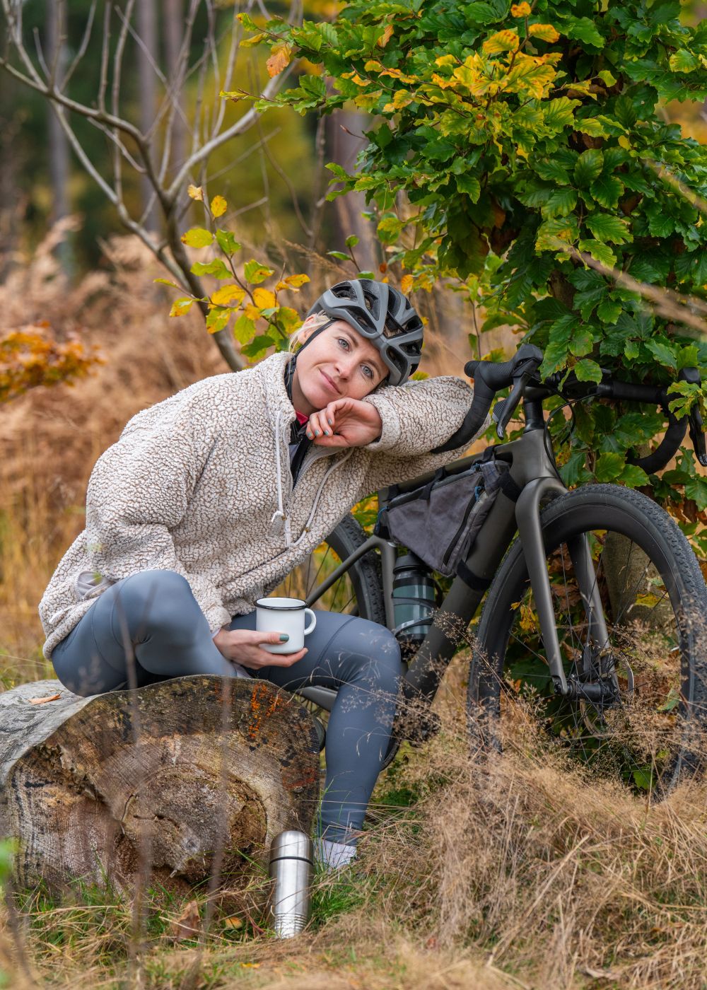 Woman holding a coffee mug and smiling during a coffee break while mountain biking