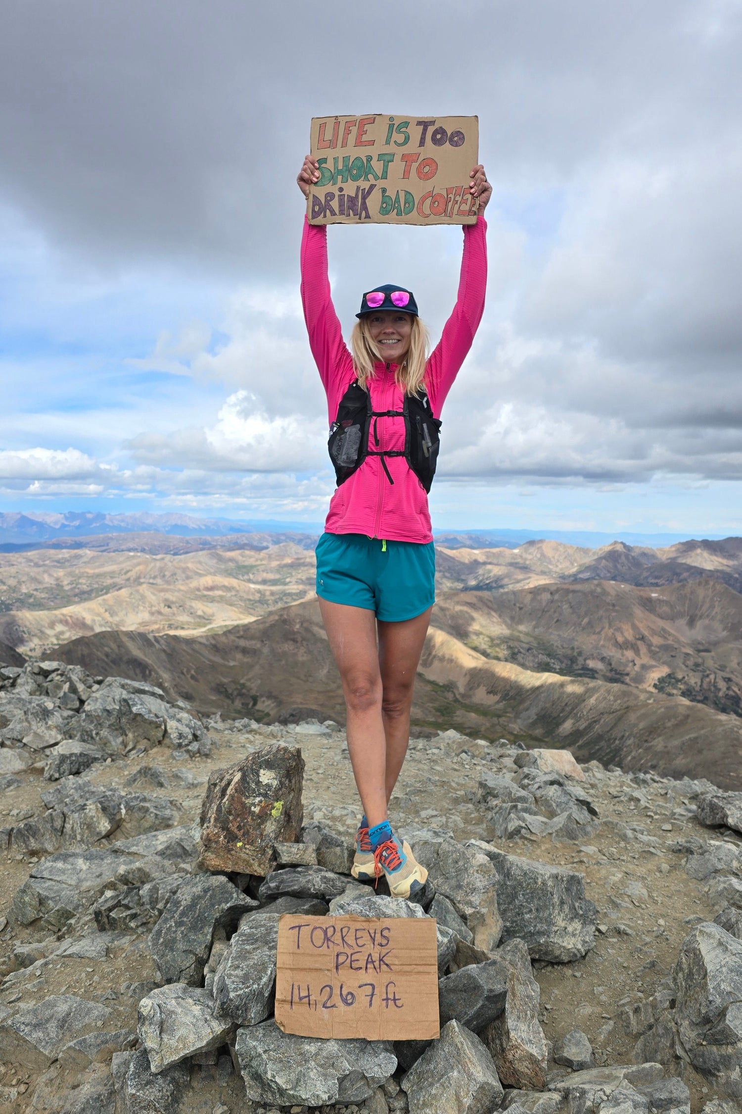 Erica Leafe on top of Torreys Peak, Colorado, holding a sign saying Life is too short to drink bad coffee