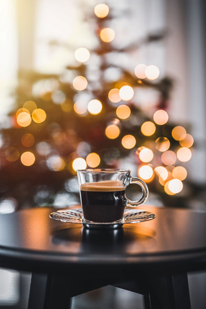 A cup of Tropical Bear Santa's Favorite Blend Specialty Coffee on a table with a Christmas tree in the background. 