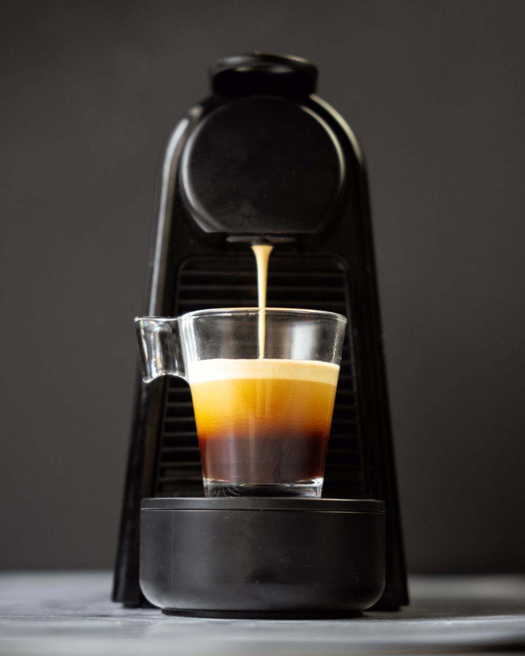 Black coffee machine pouring espresso into a glass on a dark background