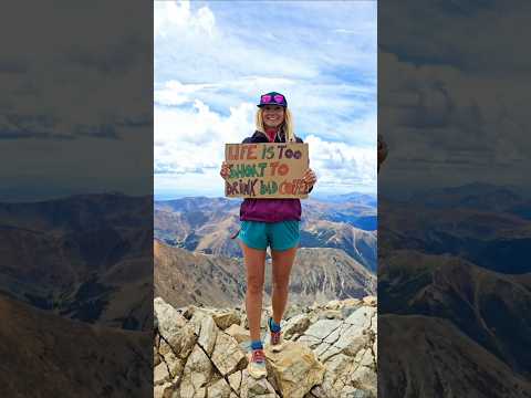 Erica Leafe at the top of a Colorado 14er holding a sign saying "Life is too short to drink bad coffee"